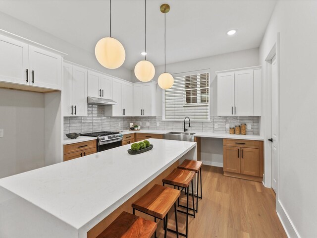 kitchen with decorative light fixtures, stainless steel gas stove, sink, white cabinets, and a center island