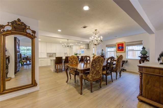 dining room with an inviting chandelier, a textured ceiling, and light hardwood / wood-style floors