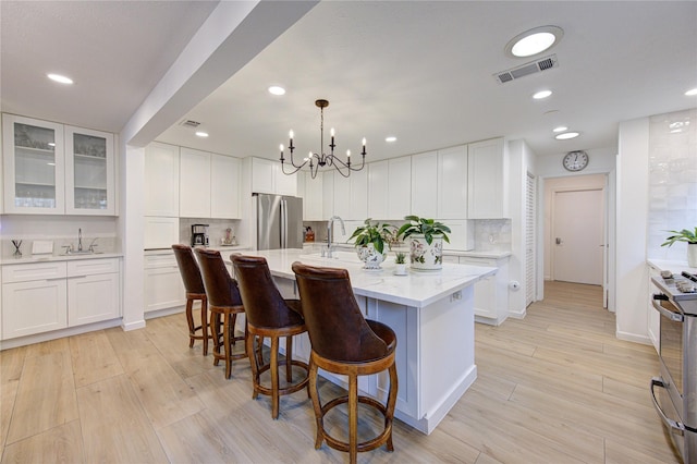 kitchen with an island with sink, appliances with stainless steel finishes, sink, and white cabinets