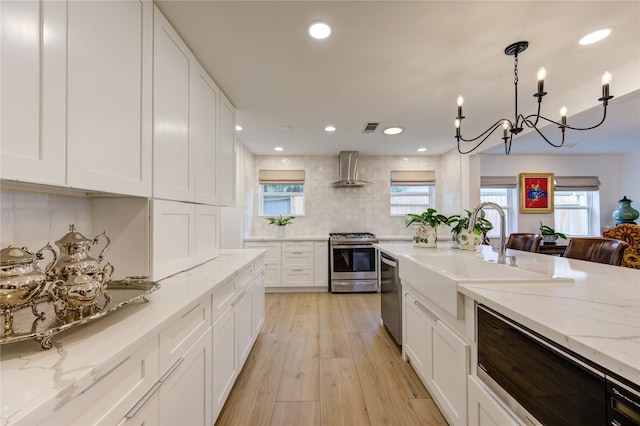 kitchen featuring appliances with stainless steel finishes, decorative light fixtures, sink, white cabinets, and wall chimney range hood