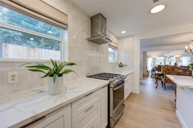 kitchen featuring an inviting chandelier, backsplash, white cabinets, gas range, and wall chimney exhaust hood