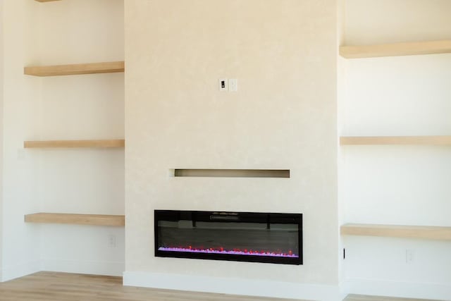 room details with baseboards, wood finished floors, and a glass covered fireplace