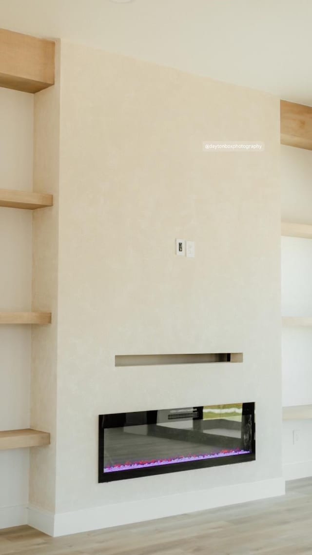 details with a glass covered fireplace, wood finished floors, and baseboards