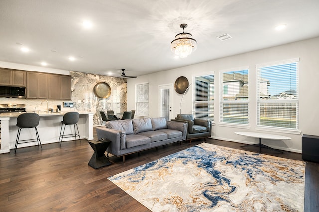 living area with ceiling fan with notable chandelier, dark wood-style flooring, plenty of natural light, and visible vents