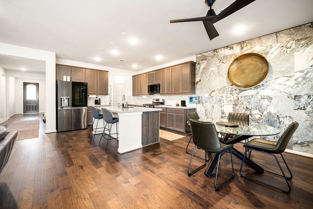 kitchen featuring dark wood finished floors, an island with sink, appliances with stainless steel finishes, a kitchen breakfast bar, and light countertops