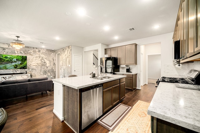 kitchen with visible vents, light stone countertops, a kitchen island with sink, stainless steel appliances, and a sink