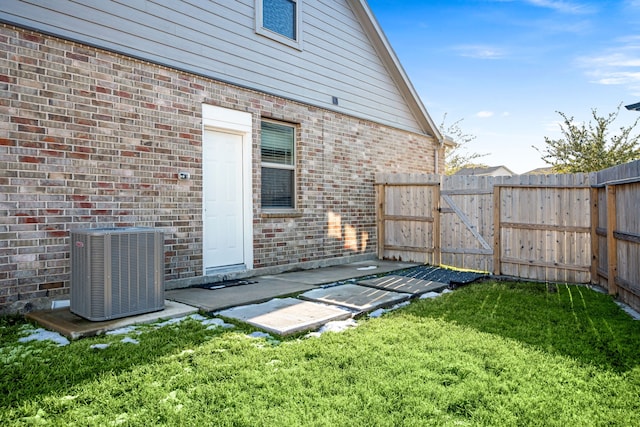 rear view of property featuring brick siding, a yard, a gate, central AC, and fence