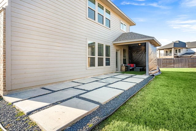 rear view of house with roof with shingles, fence, a lawn, and a patio