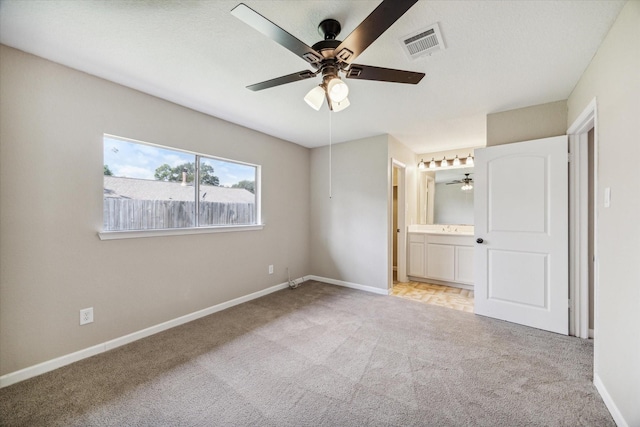 unfurnished bedroom with ensuite bathroom, sink, ceiling fan, light carpet, and a textured ceiling