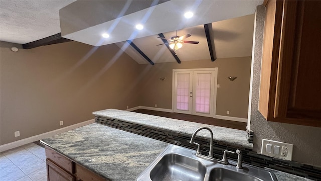 kitchen with dark stone countertops, sink, vaulted ceiling with beams, and ceiling fan