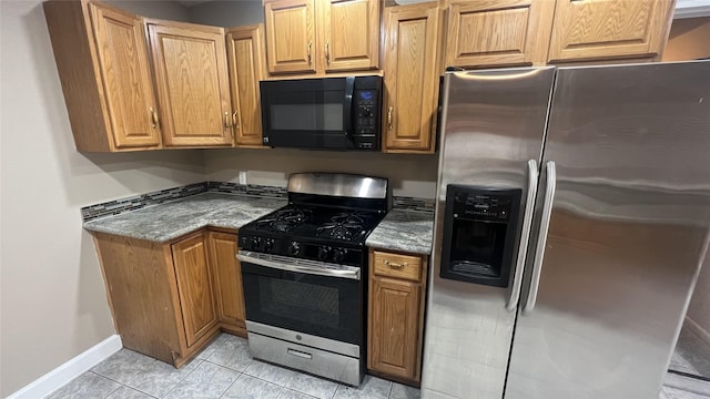 kitchen with stainless steel appliances, light tile patterned floors, and dark stone countertops