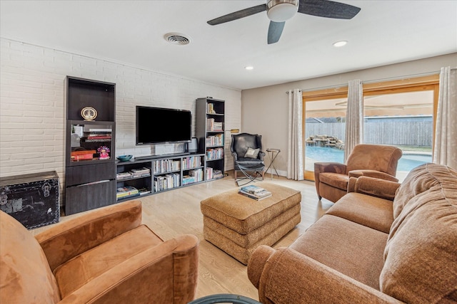 living room featuring ceiling fan, brick wall, a fireplace, and light wood-type flooring