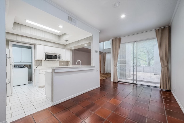 kitchen with ornamental molding, white cabinets, dark tile patterned flooring, washer / dryer, and kitchen peninsula