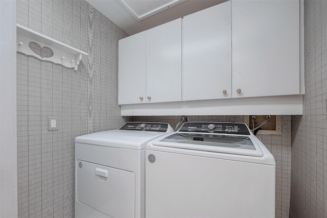 washroom with cabinets, tile walls, and washing machine and clothes dryer