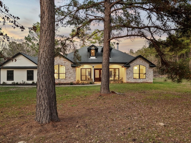 french country home with stone siding and a lawn