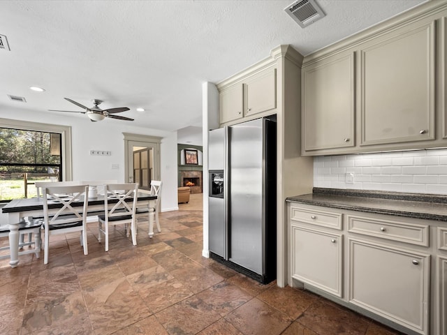 kitchen with visible vents, cream cabinetry, stainless steel refrigerator with ice dispenser, dark countertops, and decorative backsplash