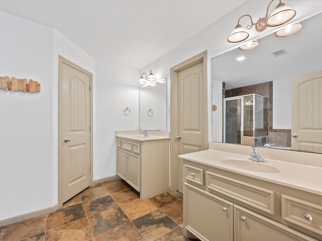 full bath featuring visible vents, a shower stall, two vanities, and a sink