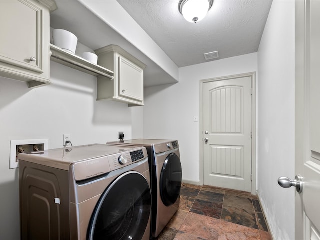 washroom with stone finish floor, washer and dryer, a textured ceiling, cabinet space, and baseboards