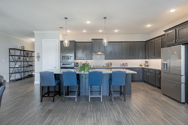 kitchen featuring pendant lighting, appliances with stainless steel finishes, a kitchen breakfast bar, tasteful backsplash, and an island with sink