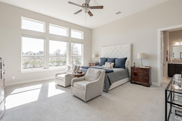 bedroom with ensuite bathroom, light colored carpet, and ceiling fan