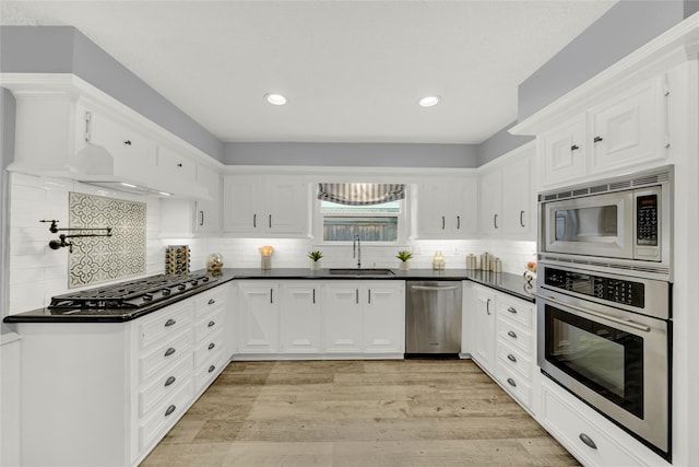 kitchen featuring appliances with stainless steel finishes, white cabinetry, sink, backsplash, and light hardwood / wood-style floors