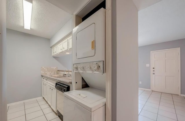 washroom with light tile patterned flooring, stacked washer and clothes dryer, sink, and a textured ceiling