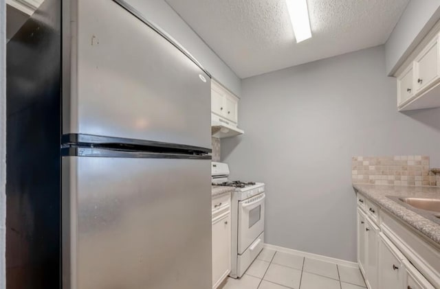 kitchen featuring white cabinetry, tasteful backsplash, light tile patterned floors, stainless steel refrigerator, and white gas range