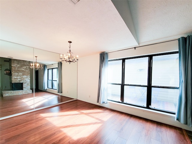 unfurnished living room with a fireplace, a chandelier, hardwood / wood-style floors, and a textured ceiling