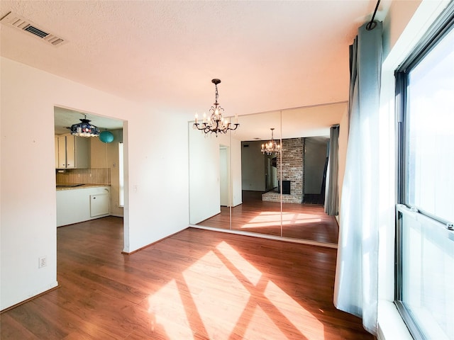 empty room with hardwood / wood-style flooring, a brick fireplace, a notable chandelier, and a textured ceiling