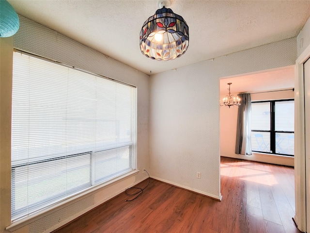 empty room featuring a healthy amount of sunlight, hardwood / wood-style flooring, a textured ceiling, and a chandelier