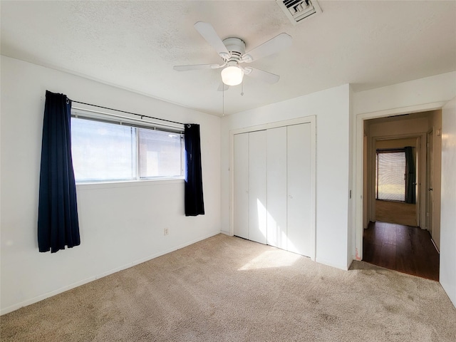 unfurnished bedroom featuring ceiling fan, light colored carpet, a textured ceiling, and a closet