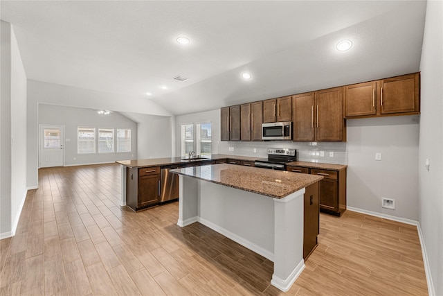 kitchen featuring dark stone counters, lofted ceiling, light wood-style flooring, appliances with stainless steel finishes, and a peninsula