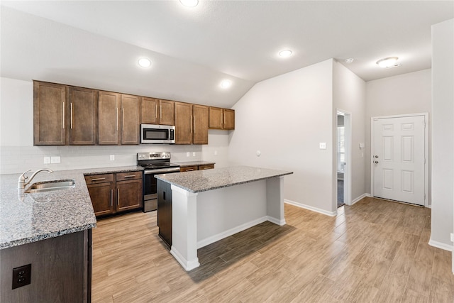 kitchen with stainless steel appliances, a sink, light wood-style flooring, and light stone counters