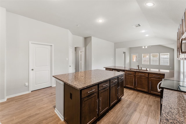 kitchen featuring a kitchen island, vaulted ceiling, a sink, and light wood finished floors