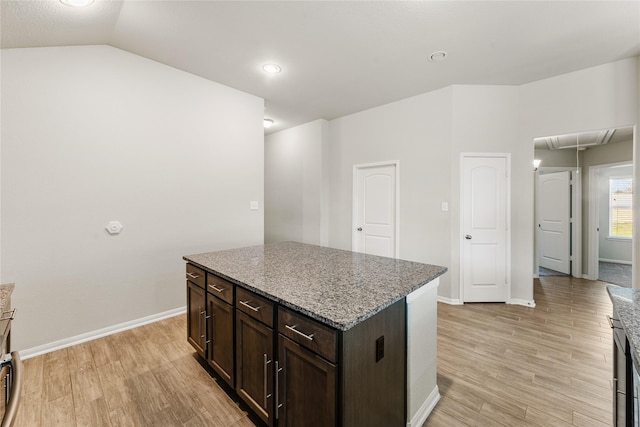 kitchen with a center island, vaulted ceiling, dark brown cabinets, light wood-type flooring, and light stone countertops