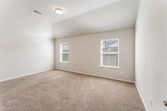 unfurnished room featuring lofted ceiling, a wealth of natural light, light carpet, and visible vents