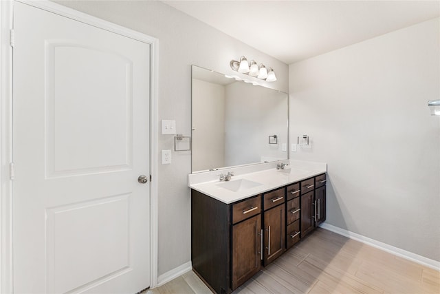 bathroom with double vanity, baseboards, a sink, and wood finished floors