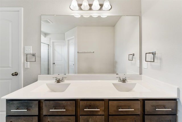 bathroom with double vanity, an enclosed shower, visible vents, and a sink