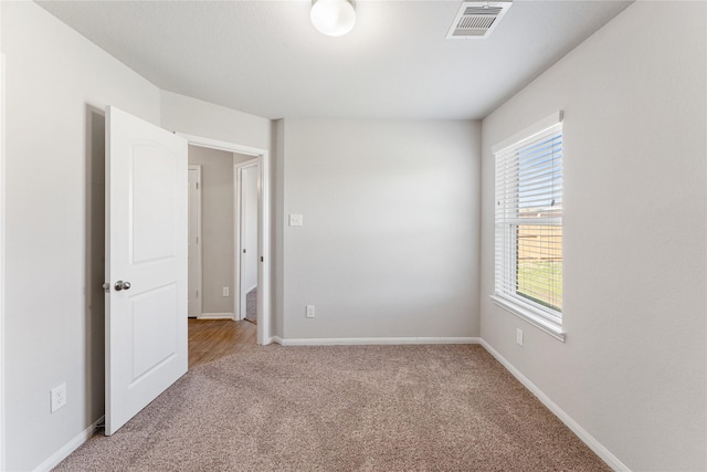 empty room with baseboards, visible vents, and light colored carpet