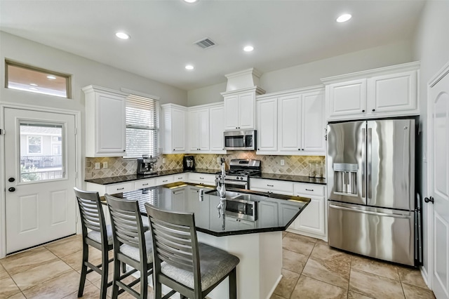 kitchen featuring tasteful backsplash, an island with sink, white cabinets, a kitchen bar, and stainless steel appliances