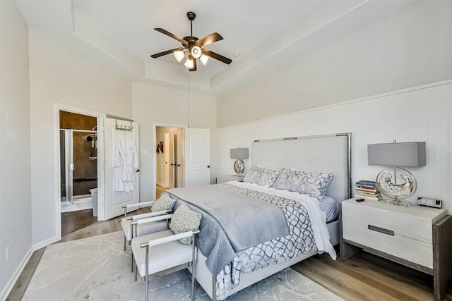 bedroom featuring a tray ceiling, wood-type flooring, ceiling fan, and a towering ceiling