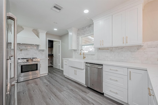 kitchen with sink, white cabinetry, light wood-type flooring, custom range hood, and stainless steel appliances