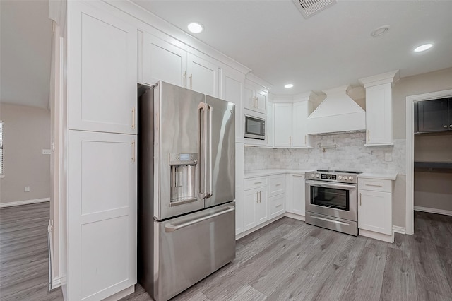 kitchen featuring premium range hood, light hardwood / wood-style floors, white cabinets, and appliances with stainless steel finishes