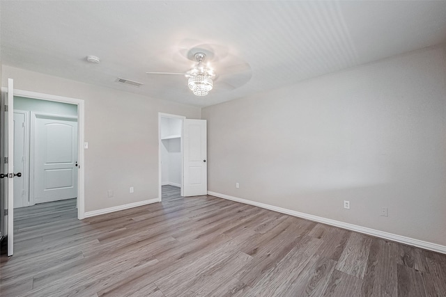 unfurnished bedroom with ceiling fan, a spacious closet, a closet, and light wood-type flooring