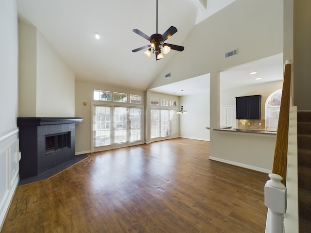 unfurnished living room with a tiled fireplace, dark wood-type flooring, high vaulted ceiling, and ceiling fan