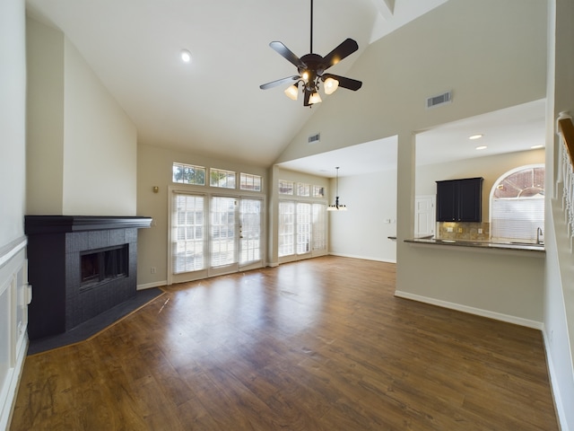 unfurnished living room with a tile fireplace, dark wood-type flooring, ceiling fan, and high vaulted ceiling