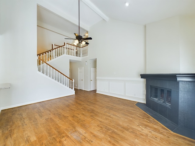 unfurnished living room with high vaulted ceiling, a tile fireplace, hardwood / wood-style flooring, ceiling fan, and beam ceiling