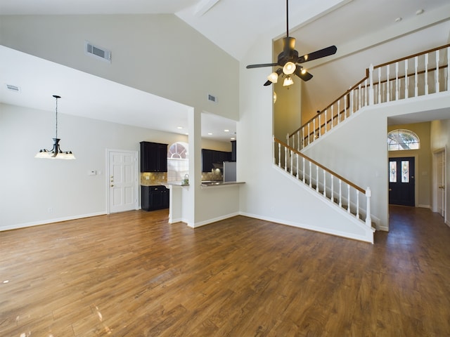 unfurnished living room with high vaulted ceiling, dark hardwood / wood-style floors, and ceiling fan with notable chandelier