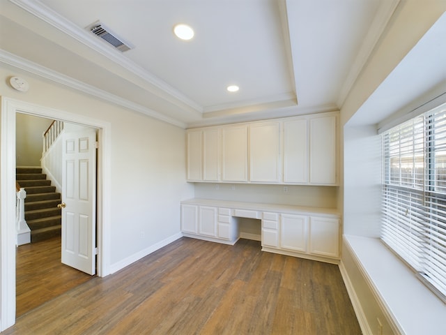 unfurnished office with a raised ceiling, crown molding, dark wood-type flooring, and built in desk