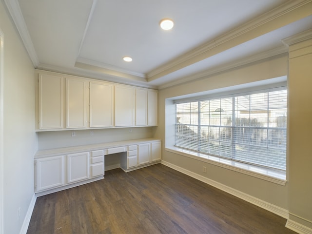 unfurnished office featuring crown molding, a tray ceiling, built in desk, and dark wood-type flooring